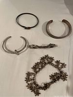 Five silver bracelets arranged on a flat surface showing various styles and tarnished condition.