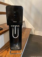 Front side of black SodaStream machine with carbonation tube visible and textured front panel.