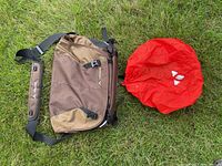 Brown and tan VAUDE Tecoleo L shoulder bag and red rain cover displayed on grass
