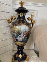 Front view of large decorative Limoges vase showing navy blue base with gold decorative elements and central pastoral scene.