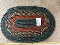 Close-up of a medium oval braided rug with dark green, brown, and tan colors showing braided texture and seller's lot tag.