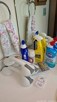 Photo of bathroom cleaning supplies including Lysol, Clorox, Cameo powder container, Bath & Kitchen cleaner spray bottles, white shower grab bars, and floral towels.