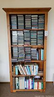 Front view of tall wooden bookshelf filled with music CDs and books, showing size, shelves, and content arrangement.