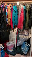 Assortment of men's and women's coats on hangers with some clothing bags below and cushions.