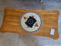 Top view of rectangular wooden coffee table with scalloped edges and a decorative doily on top. The finish is medium brown with visible wear.
