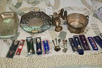 Wide view of the collection including trays, pitcher, bucket, and boxed souvenir spoons laid out on fabric surface.