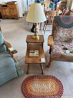 Wooden tiered side table with brass lamp, coasters on bottom shelf, flanked by armchairs in living room setting.