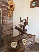 Wooden spinning wheel beside two ceramic vases on brick hearth.