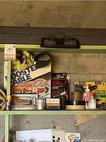 Close-up of top shelf featuring cooler, 3-piece 'C' clamp set, Craftsman drill bit set, pistol grip stapler, tape rolls, and small hardware boxes.