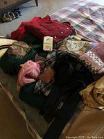 Photo showing a collection of wool sweaters in various colors, vintage scarf and gloves on a bed