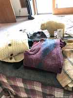 Folded wool sweaters in various colors alongside a small wool bear on a plaid surface
