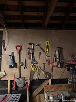 Full view of pegboard with many tools including saws, shovel, clamps, hammer, spirit level, and power sander.