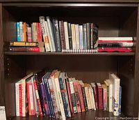 Two shelves of assorted books including John Grisham novels, cookbooks, and home repair books, arranged on dark wood shelves.