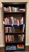 Front view of wooden bookcase filled with books showing dimensions and condition.