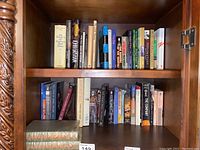 First image showing one shelf of a wooden bookshelf filled with various mixed books of different sizes and colors.