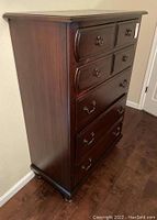 Angle view showing the full height and side profile of the dark wooden chest of drawers with five drawers and metal handles.