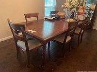 Full view of the rectangular dining table with six chairs around. Table shows dark wood finish and surface wear.