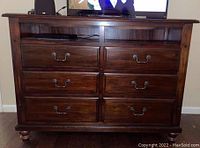 Front view of wooden dresser with six drawers and two open compartments on top, dark brown finish, metal handles, standing on rounded feet.