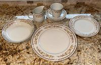 Photo showing various china pieces including cups, a creamer, saucers, plates, and bowls with floral golden autumn pattern.