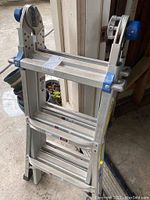 Side view of folded aluminum Werner ladder showing blue plastic hinge knobs and aluminum rungs.