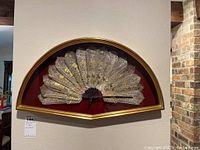 Full view of framed Spanish decorative fan mounted on burgundy backing inside a curved gold frame, showing fan spread wide.