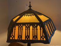Close-up of stained glass amber panels with ornate dark metal framing and finial on top of lamp shade
