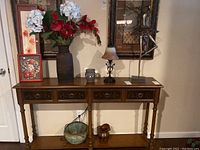 Photo showing a wooden table with metal art ballerina sculpture, table lamp with glass shade, pottery wax warmer, large wood vase with faux florals, and smaller metal and wood vases