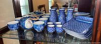 Full set of blue floral teapot with cups, saki servers, saki cups and divided plates arranged on glass shelf