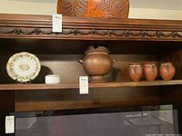 Full shelf view showing three small terracotta pots, large soup tureen, decorative floral plate with stand, and Otagiri porcelain cat trinket box.
