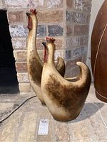 Two clay pottery chicken-shaped planters displayed on floor against brick wall, one larger behind smaller, showing general size and condition including surface texture and paint