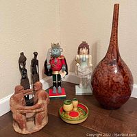 Overview of the lot showing all items together on the floor corner including the pottery vase, oil & vinegar dish, nutcrackers, carved figures, and pottery circle sculpture.