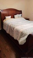 Full view of queen size sleigh bed with bedding against beige wall on wooden floor.