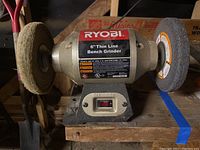 Front view showing grinder with polishing and grinding wheels, mounted on wooden bench.