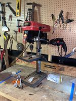 Skill model 3320 drill press angled view showing base, column, worktable, and drill head. Workbench and hand tools in background.