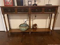 Full front view of wooden sofa table showing four drawers with floral inlays and ring pulls, bottom shelf, and turned legs.