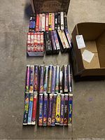 Photo showing approximately 30 VHS tapes arranged on the floor with visible titles mainly from Disney's animated movies and collections.