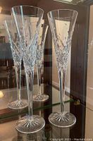 Two tall Waterford crystal champagne flutes displayed on glass shelf, showing detailed cut crystal designs and starburst bases.