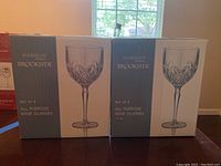Two unopened boxes each containing four Marquis by Waterford Brookside all-purpose wine glasses, labeled clearly with branding and pattern details.