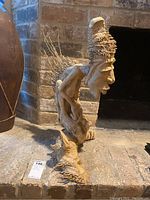 Side view showing detailed facial features, headdress, and twig-like accents at the back.