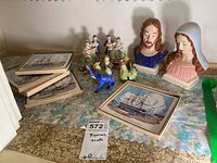 Photo shows all items on a surface including 4 wooden Old Ironsides ship trivets stacked to the left, ceramic figurines of various types including musicians and animals in the center, and two larger ceramic busts of religious figures to the right.