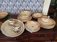 Overview of the full 20 piece set laid out including plates, teacups, and platter on wooden surface in front of patterned wallpaper.