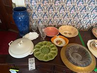 Photo showing mid-century ceramics, glassware, and blue vase on table with floral wallpaper background