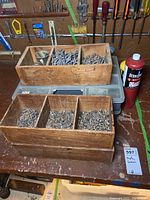 Wooden organizers displaying assorted nails and screws on a workbench, with a red flammable fluid container beside them.