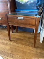 Full view of the wood nightstand showing glass top, drawer front and tapered legs.
