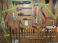 Photo showing a variety of hand tools including pipe wrenches, hand saws, pliers, screwdrivers neatly arranged on a pegboard