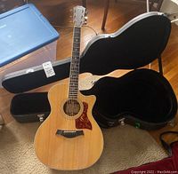 Full view of guitar standing next to open hard-shell case on floor