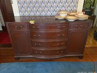 Front view of vintage Paines of Boston wooden buffet showing three curved front drawers in center and cabinet doors on each side, dark wood finish, scratches and stains on top.