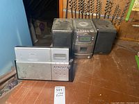 Photo showing Panasonic radio, JVC CD player and speakers covered in dust on wooden floor with drill bits in background