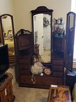 Full front view of the antique solid wood dressing vanity showing central mirror, side mirrors, drawers and surface with decorative dolls.