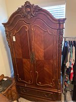 Full front view of the large wooden solid wood armoire with carved floral and scroll details on the doors and top.